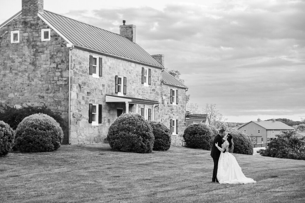 A black and white picture of a man and woman kissing in front of a house