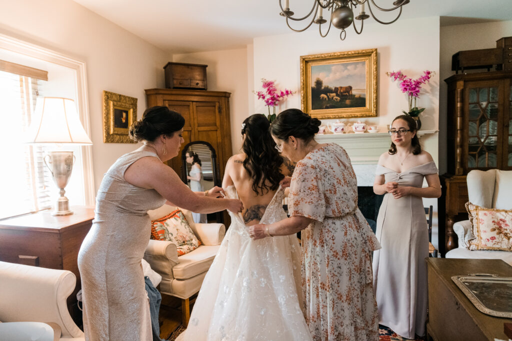 Two women helping another woman zip up the back of her wedding dress