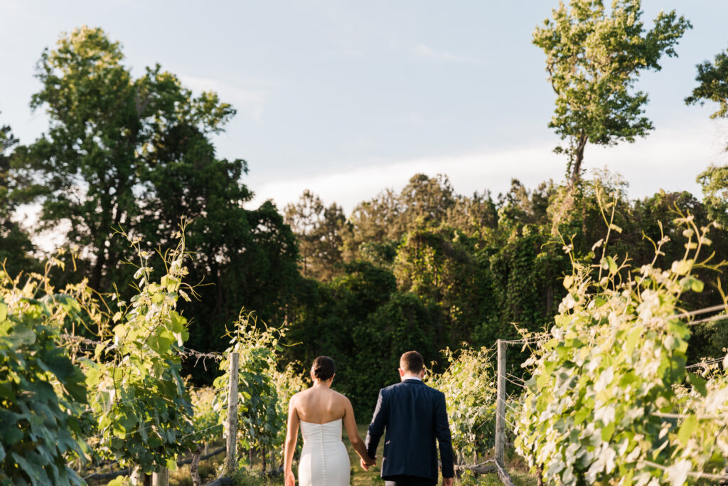 A bride and groom walking through a vineyard holding hands