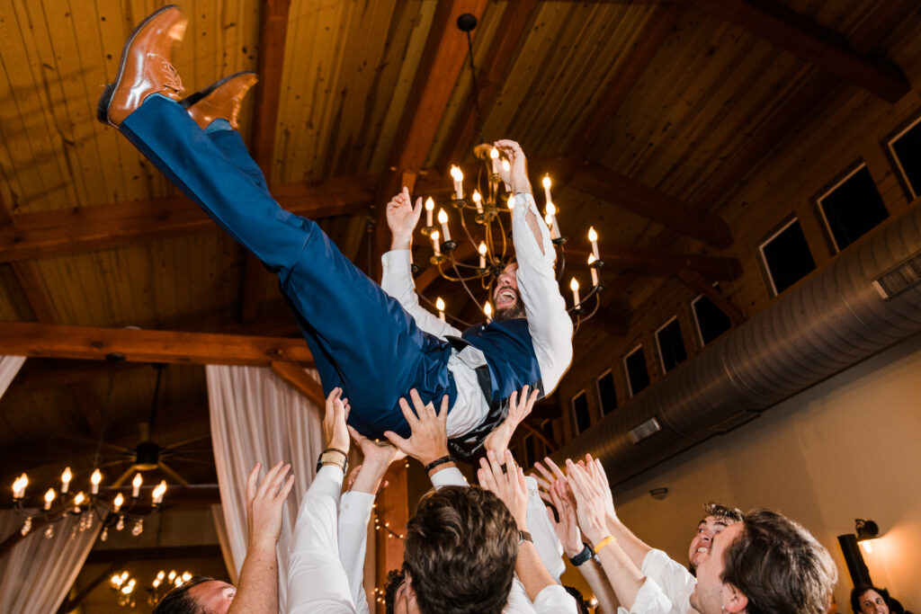 A groom being thrown up in the air by guests during a wedding reception