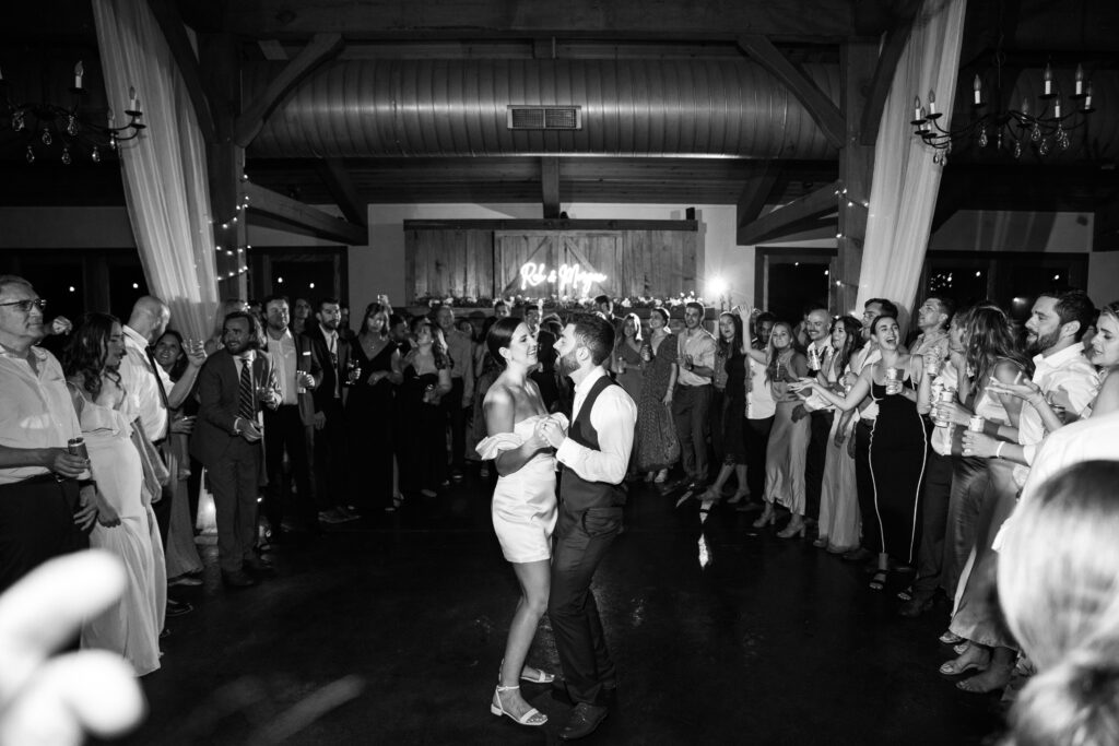 A bride and groom dancing as their wedding guests surround them.