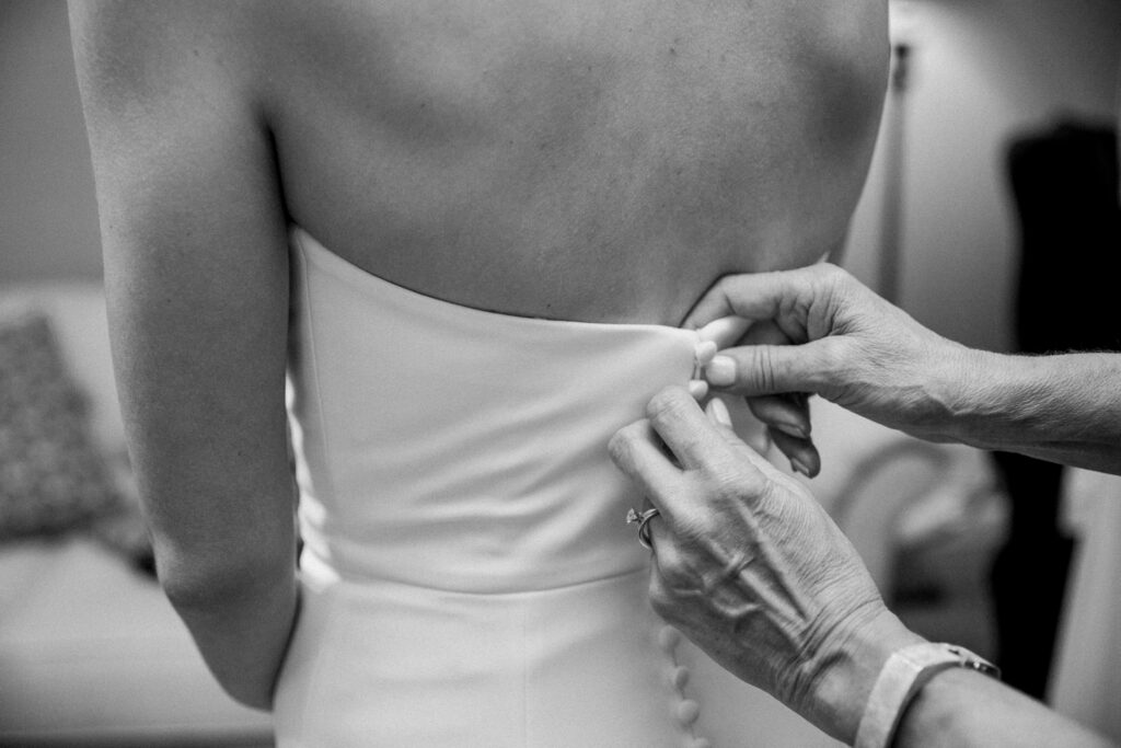 The back of a bride's wedding dress being buttoned up.