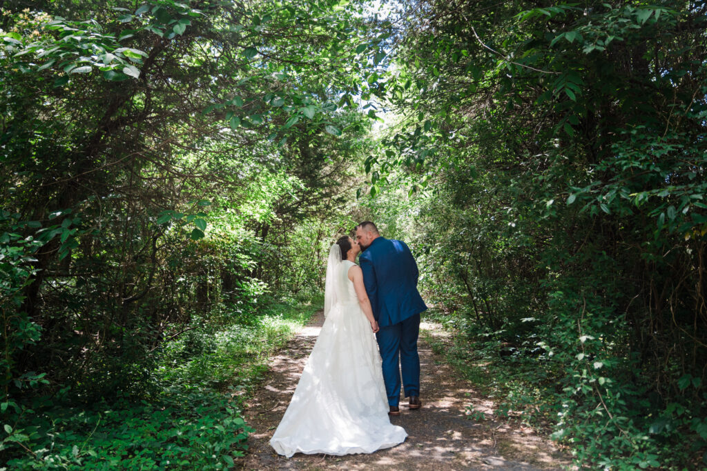 A bride and groom kissing in the woods with their backs to the camera