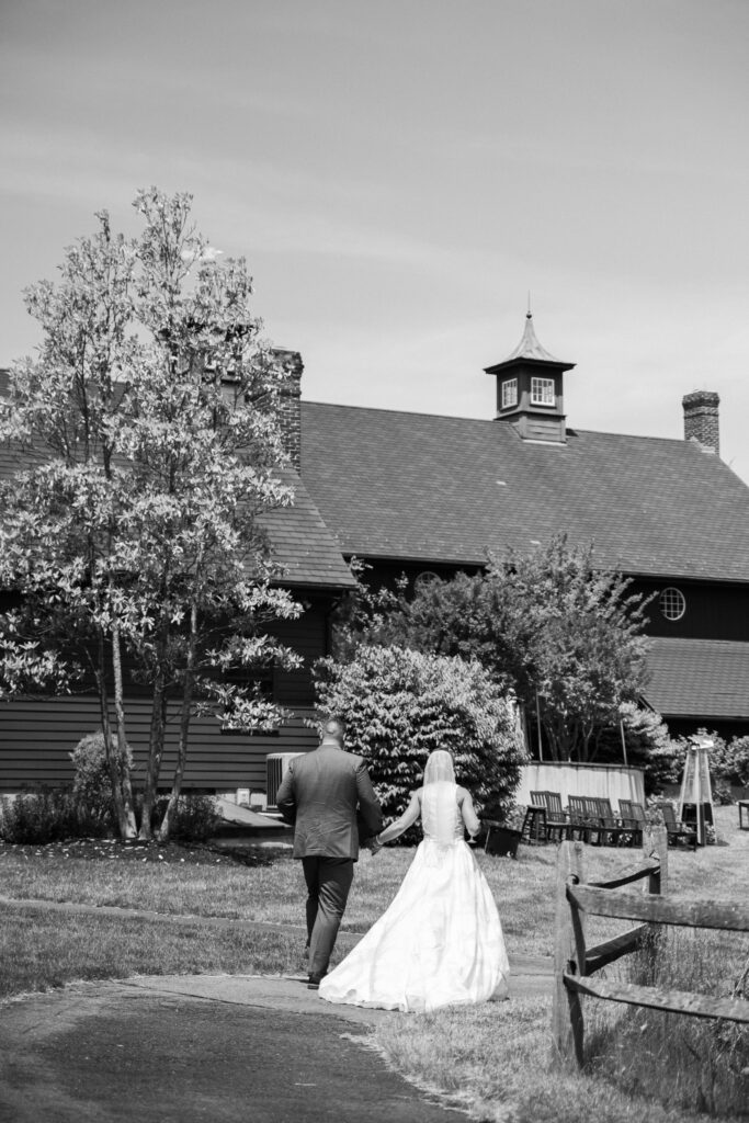 Black and white picture of a bride and groom walking in a field with their backs to the camera