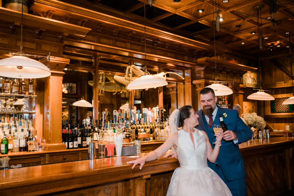 Bride and groom standing at a bar cheersing drinks