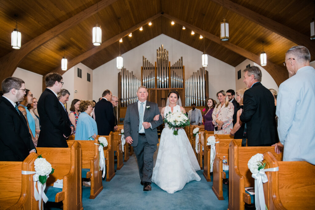 A bride walking down the aisle of a church holding the arm of a man.